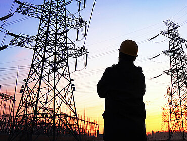 Mann steht vor Strommasten in der Abenddämmerung