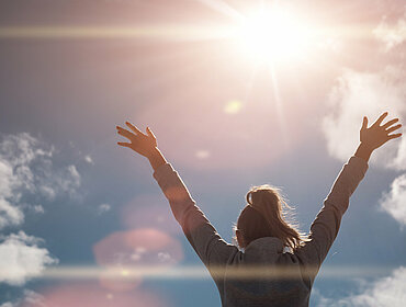 Glückliche Frau hebt die Hände zur Sonne