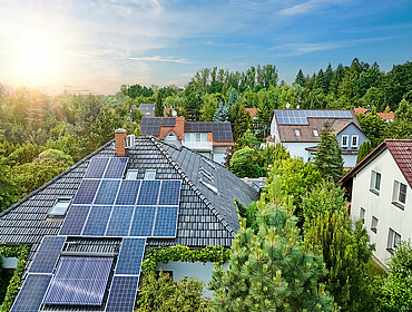 Luftaufnahme der Dächer von Häusern. Einfamilienhäuser in Gärten, Photovoltaik-Paneele auf dem Dach, Sommer, blauer Himmel mit untergehender Sonne.