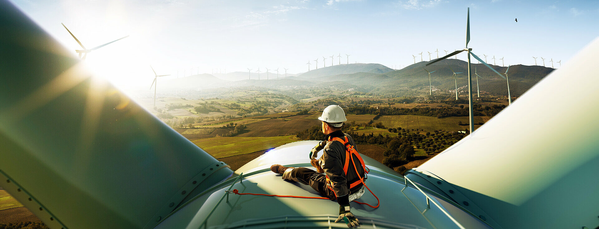 Windkraft Ein glücklicher Ingenieur, der sich nach gelungener Arbeit über seinen Erfolg freut. Er steht oben auf einer Windkraftanlage und blickt auf eine schöne Sonnenuntergangslandschaft.