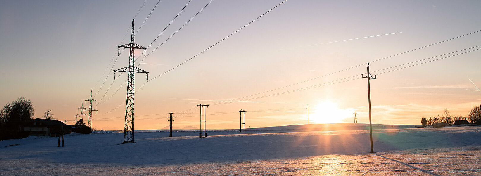 Electrical tower on a snowy field. Sun goes down, orange colors, Strommast Winterlandschaft Österreich