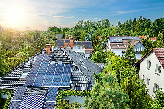 Luftaufnahme der Dächer von Häusern. Einfamilienhäuser in Gärten, Photovoltaik-Paneele auf dem Dach, Sommer, blauer Himmel mit untergehender Sonne. 