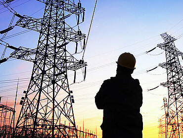 Mann steht vor Strommasten in der Abenddämmerung